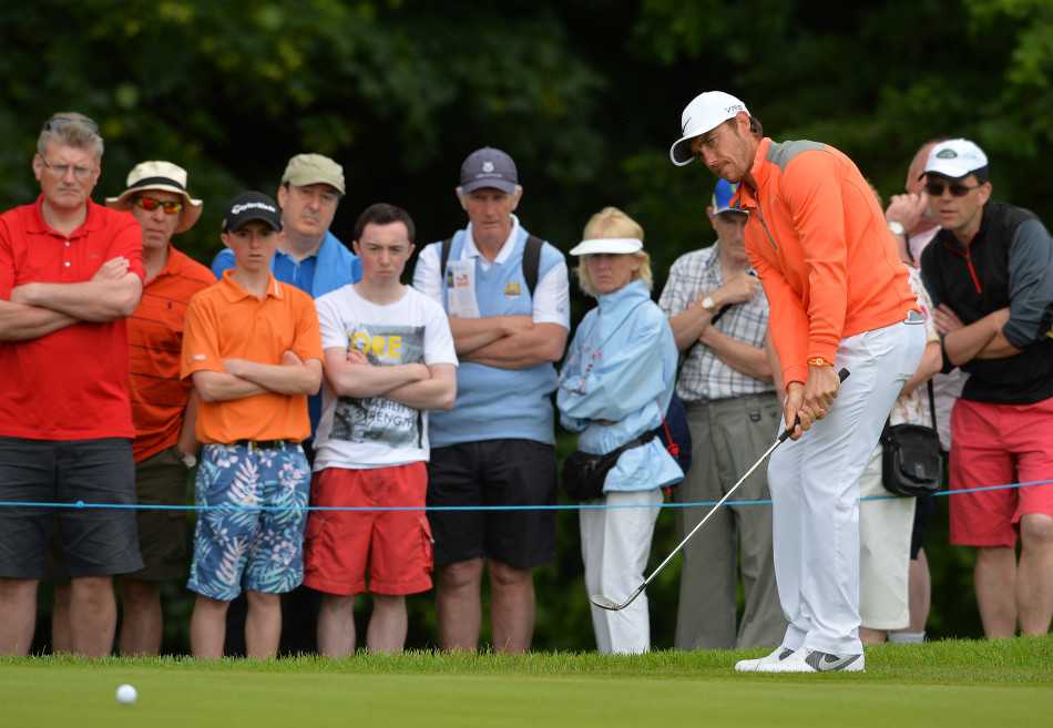 帕德里克·哈灵顿在为特殊奥运会高尔夫球队进行教学时，身体前倾，专注地为学员示范标准的推杆动作。