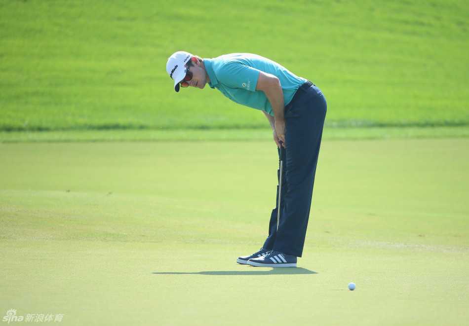 贾斯汀·罗斯在果岭上全神贯注地俯身观察推杆线路，寻找草纹的细微走向