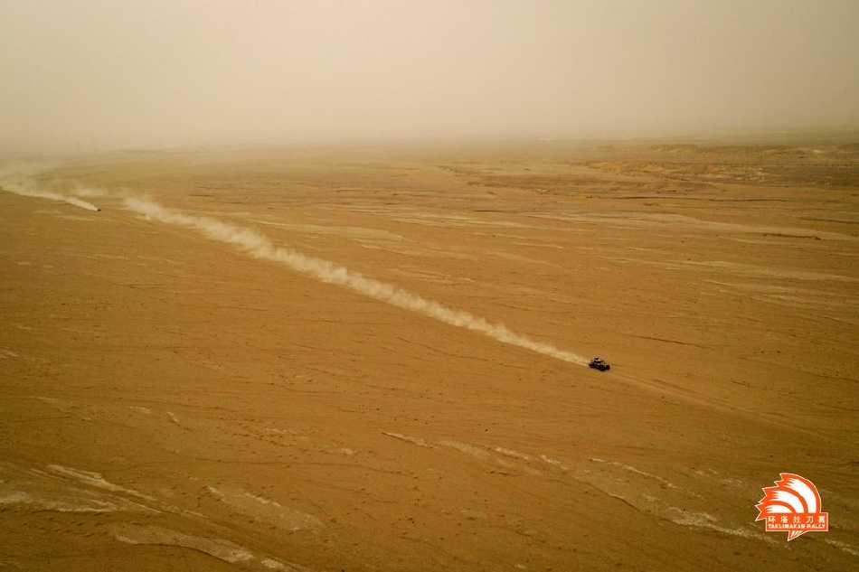 黄色涂装的越野赛车正奋力攀爬一座巨大沙山，车尾扬起漫天沙尘，在湛蓝天空下勾勒出力量与拼搏的轨迹。