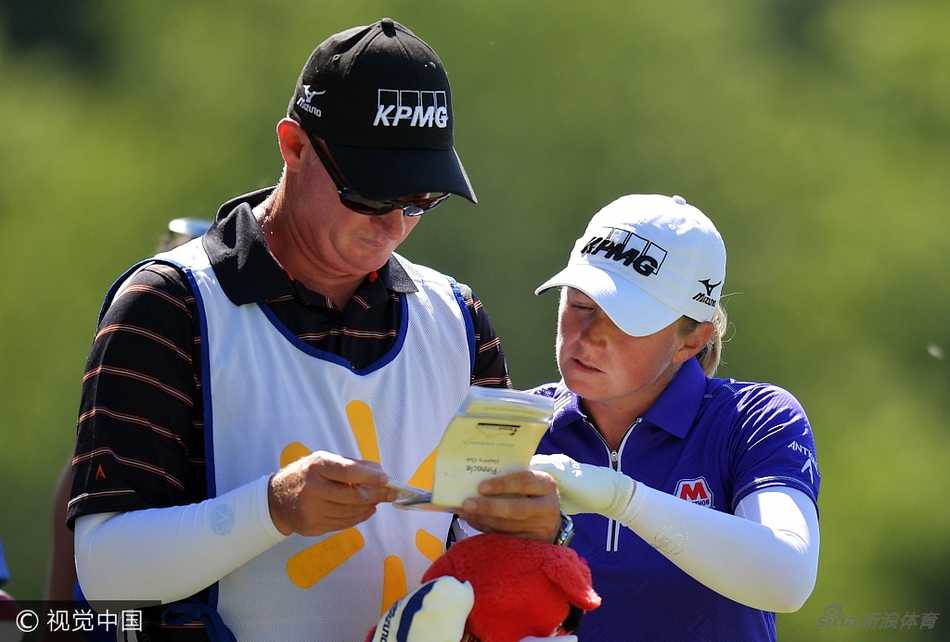 史黛西·路易斯与球童蹲在球道边，手持球场指南，神情严肃地共同商讨下一杆的进攻策略。