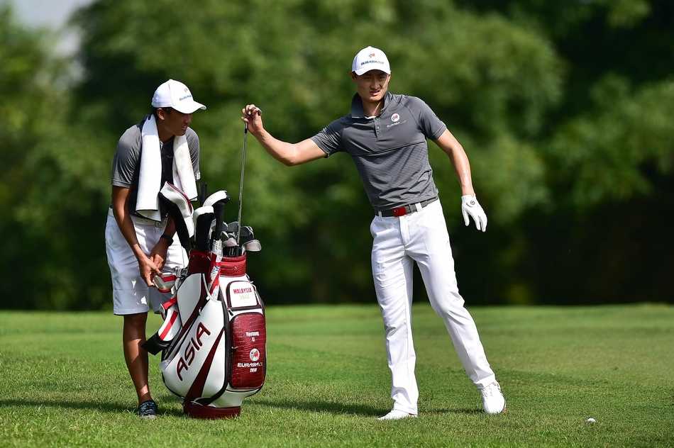 欧亚杯赛前风云:高尔夫悍将齐聚吉隆坡 亚洲队副队长张连伟目光如炬,正为队员进行战术指导,身后是郁郁葱葱的热带球场景观。