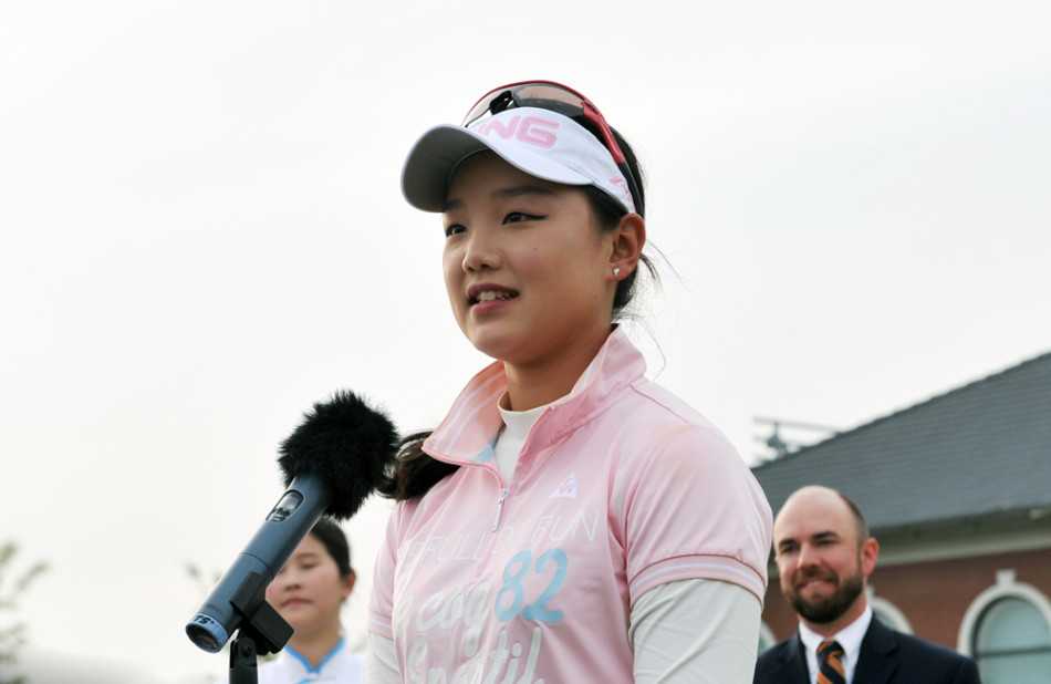 石昱婷闪耀美国女子公开赛的荣耀时刻 石昱婷手持奖牌,站在演讲台后发表获奖感言,她神情认真而谦逊,微微低头看向手中的讲稿,现场观众在背景中凝神聆听。