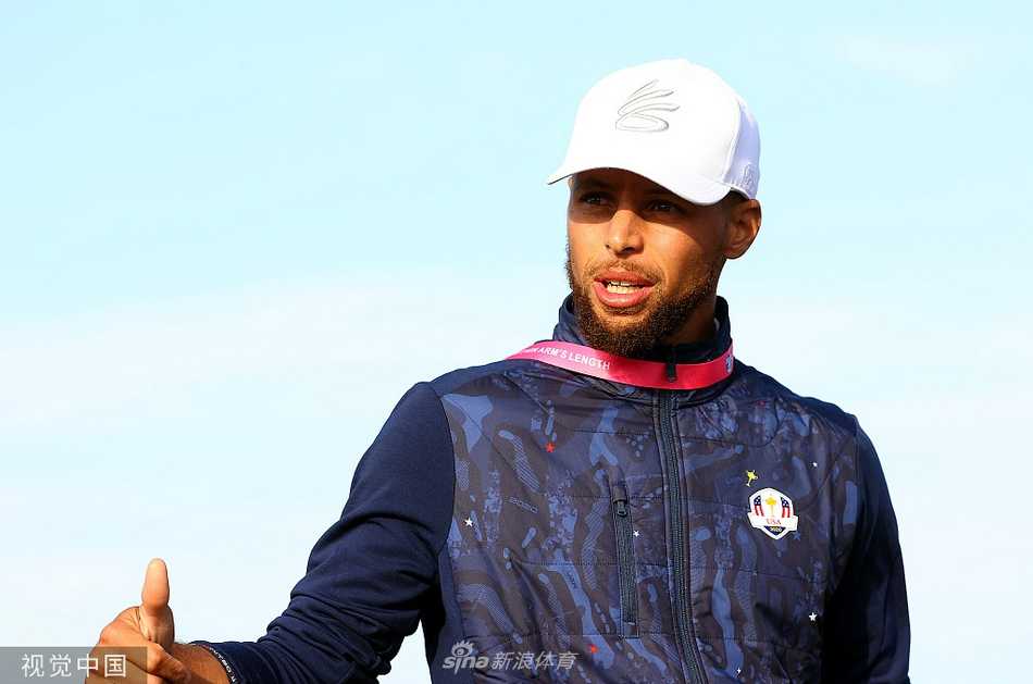 史蒂芬·库里头戴鸭舌帽，身穿美国队队服，正专注地与身旁友人就某个精彩击球瞬间展开热烈讨论，神情投入。