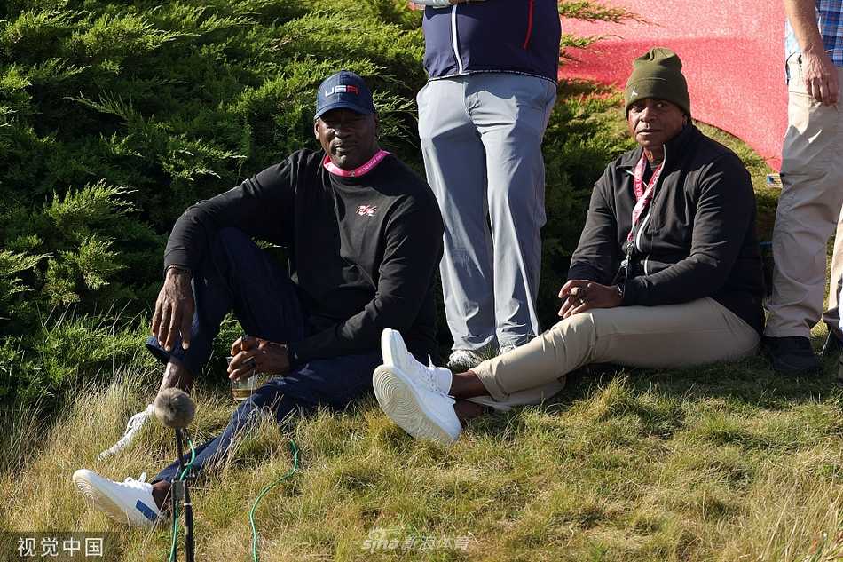 迈克尔·乔丹身着深色休闲装，双手插兜，以一种冷静而权威的姿态凝视赛场，周身散发着历经大赛洗礼的沉稳气质。