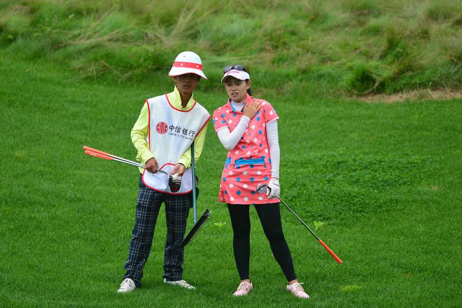 女子获奖球员与她的球童在领奖台上相视而笑，共同举起奖杯，分享这份来之不易的胜利喜悦。