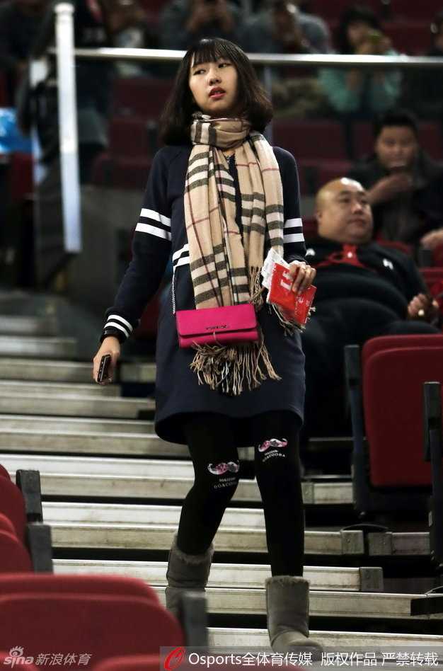 她穿着一袭黑衣显得干练十足，微微一笑间流露出对比赛的从容欣赏，仿佛在品味一场精彩的篮球盛宴。