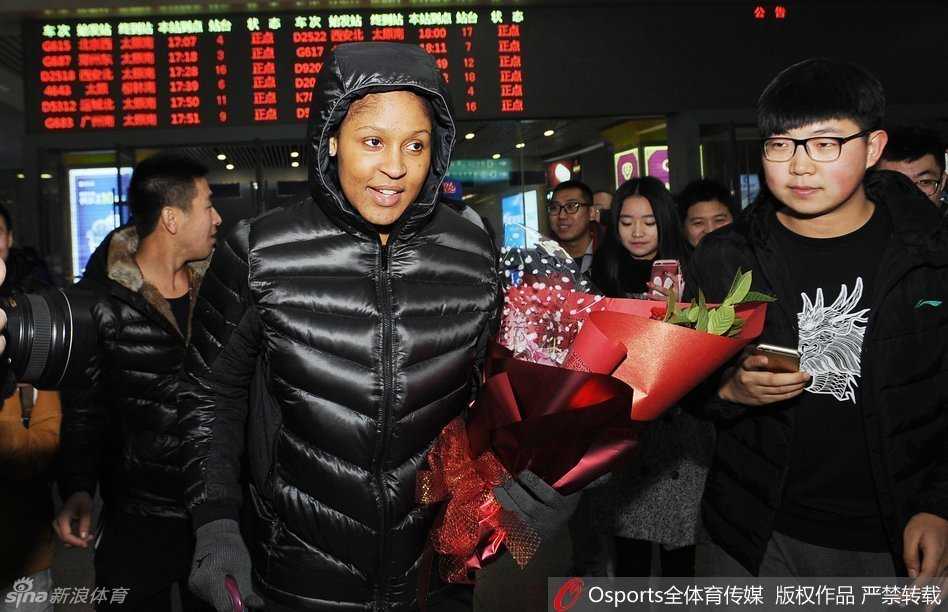 热情的山西女球迷手捧精美的鲜花，在人群中踮起脚尖，急切地将花束递到玛雅·摩尔面前，表达对她的喜爱。