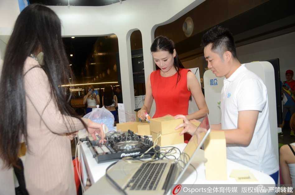 义卖现场气氛热烈，许诺双手捧着一件签名的纪念T恤递给爱心人士，脸上洋溢着真诚的感激之情，周围的闪光灯记录下这温暖的一刻。