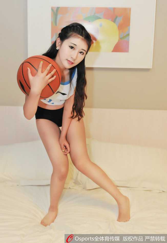 一位篮球宝贝俯身热舞，完美的身体曲线在聚光灯下展露无遗，她身后的球迷看台已是人山人海，静待德比开场。