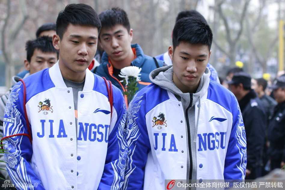 队员们排成一列，向着刻满遇难者名字的纪念碑深深鞠躬，身体几乎弯成九十度，背景是苍翠的松柏，寓意着精神不死与和平永驻。