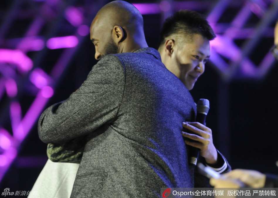 科比微微俯身，专注地为沈阳的小球员布置战术，身后的贺天举认真聆听，仿佛也回到了自己初学篮球的青涩时光。