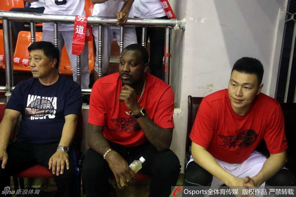 赛前热身中，新疆队球员李根目光如炬，在进行拉伸训练，他的身后是巨大的广告牌和正在入场的球迷，大战氛围一触即发。