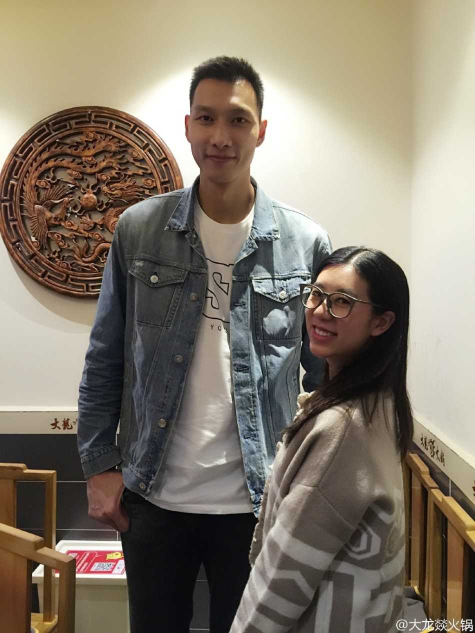 在热闹的火锅店氛围中，阿联面对镜头露出标志性的腼腆微笑。身旁的女店员因为兴奋和紧张，身体不自觉地微微前倾，她高举的手掌在阿联巨大的手掌映衬下显得格外小巧，两人掌心的贴合仿佛是对这次“偶遇”最美好的见证。