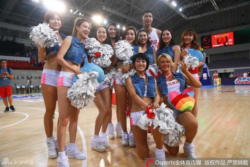 在中场休息的璀璨灯光下，一位笑容甜美的篮球宝贝手持啦啦队花球，她的身后是即将回场的中国男篮队员们，整个球馆洋溢着青春与热血的气息。