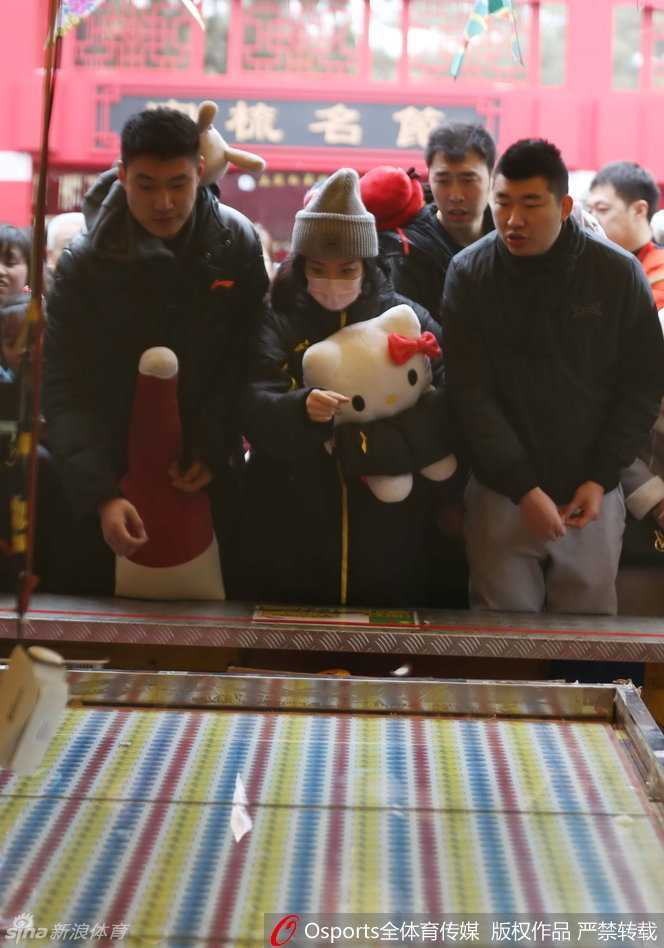 逛累了的常林与女伴在庙会休息区小憩，他手中依然抱着那个大玩偶，脸上带着些许疲惫却十分满足的神情，身后是庙会熙熙攘攘的人流和喜庆的装饰。