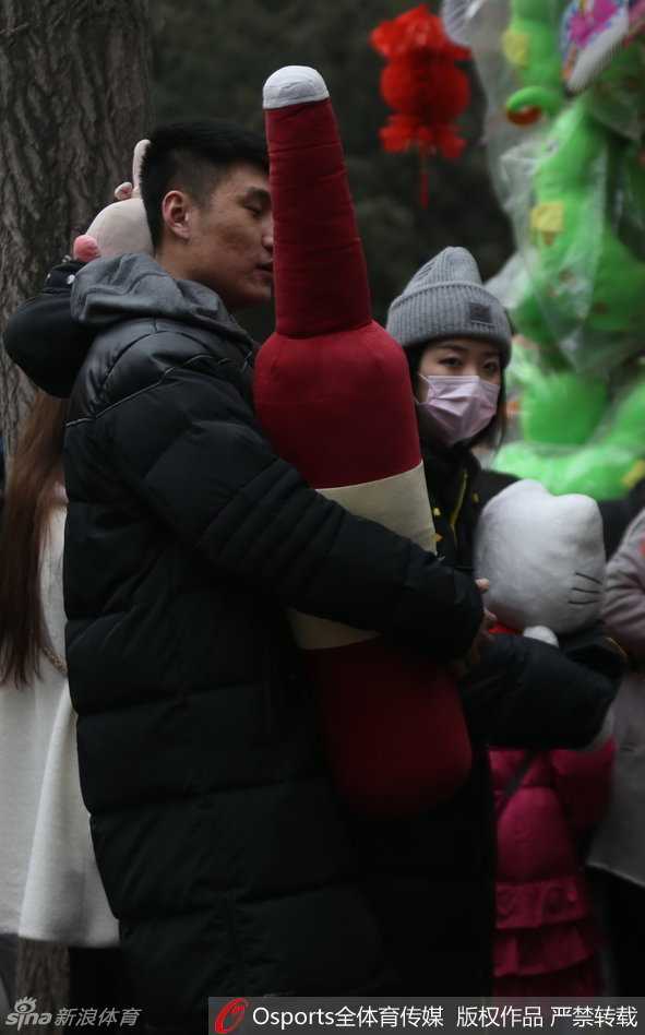 常林与女伴在一个售卖传统工艺品的地坛庙会摊位前选购，他微微低头倾听女伴的话语，205厘米的身高在人群的映衬下宛如巨人，画面充满了温馨的日常气息。