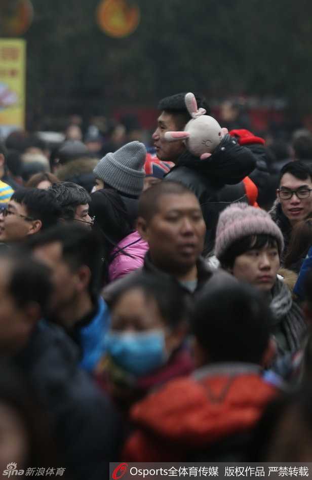 常林正全神贯注地参与庙会上的趣味游戏，他怀中抱着一个巨大的卡通毛绒玩偶，显然是刚刚获得的战利品，脸上带着轻松愉悦的笑容，尽显硬汉柔情。