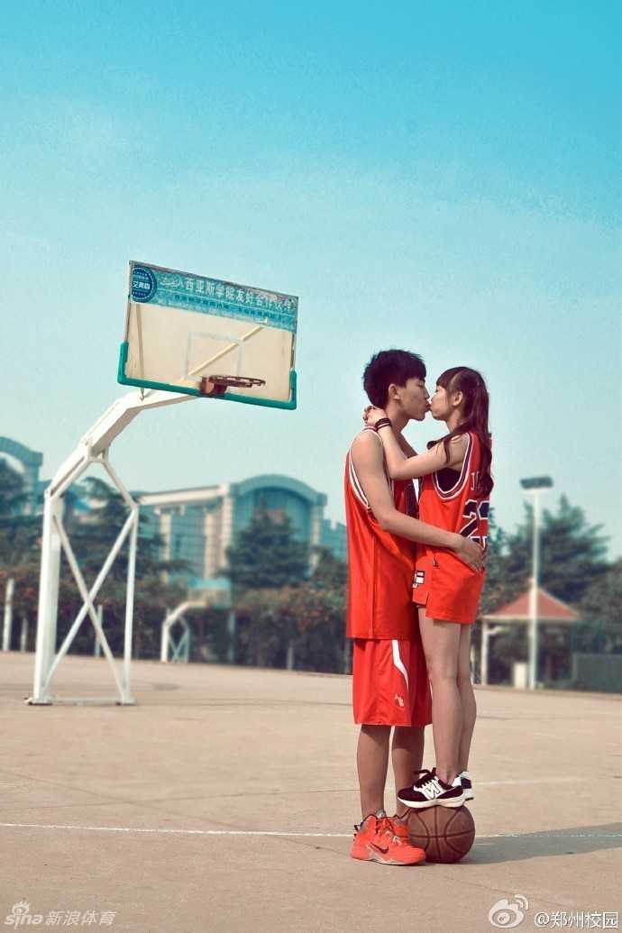 在空旷的校园篮球场上，身穿情侣球衣的女孩调皮地从背后紧紧抱住男孩，男孩双手插兜任由她抱着，两人在夕阳下享受着只属于他们的甜蜜时刻。