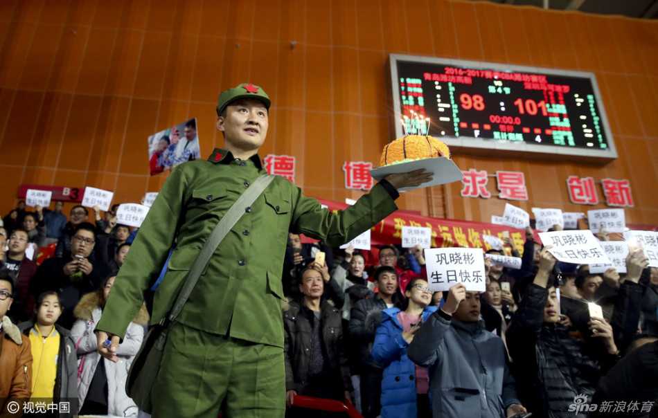 青岛队主帅巩晓彬身着深色西装站立在场边指挥，他眉头微蹙，全神贯注地盯着场上局势，右手做出战术手势，身后的看台上球迷横幅隐约可见，生日夜的这场比赛让他丝毫不敢松懈。