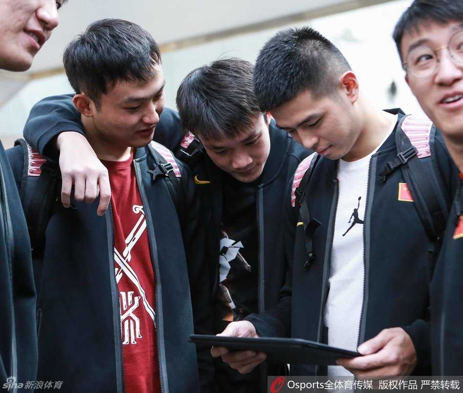 男篮队员们紧紧围拢，目光锁定屏幕上的科比告别战，队长周鹏神情专注，丁彦雨航与队友们一同沉浸在传奇的最后一舞中。