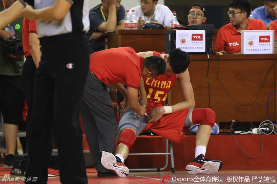 队医单膝跪地，神情专注而紧张，手中拿着喷雾剂为周琦的伤处紧急降温镇痛。周琦依旧趴在地上，只能微微抬起头，眼神中透露出难以掩饰的痛苦与不甘。