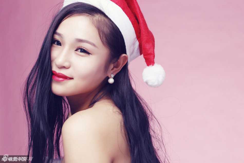 画面中的啦啦队员活力四射，她轻轻倚靠在装饰着彩球的背景板上，蓬松的白色裙摆和红色的蝴蝶结营造出浓郁的圣诞气息，俏皮的动作中透出无限的青春朝气。