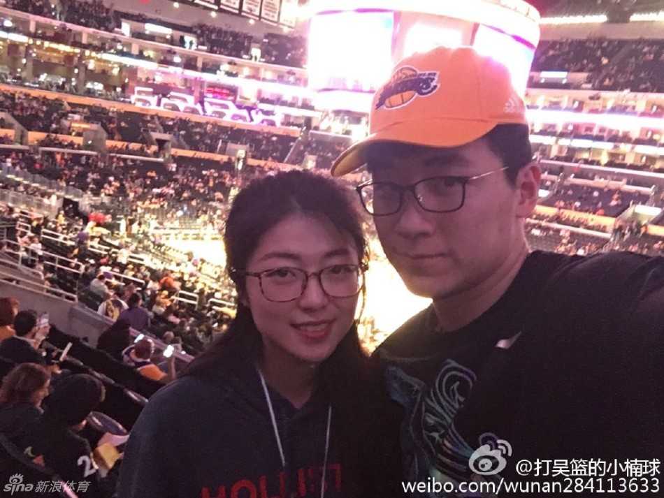 吴楠在斯台普斯中心球馆内，背对着正在热身的球场，竖起大拇指，身后的湖人队标志熠熠生辉。