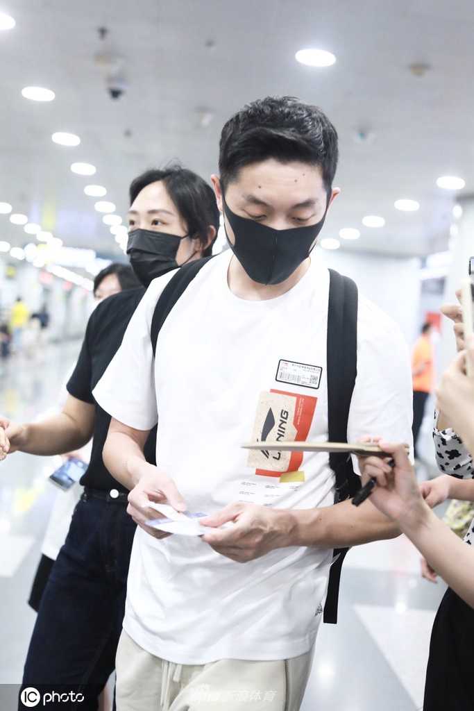 许昕戴着棒球帽和黑框眼镜，打扮休闲，正低头看着手机，似乎在处理落地后的紧要事务。