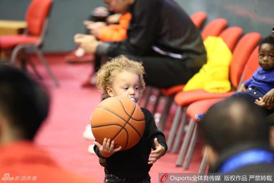 哥哥终于抱起篮球，好奇地用手指摸索着球的纹理，妈妈在一旁温柔注视，眼神里满是对孩子和丈夫的爱意