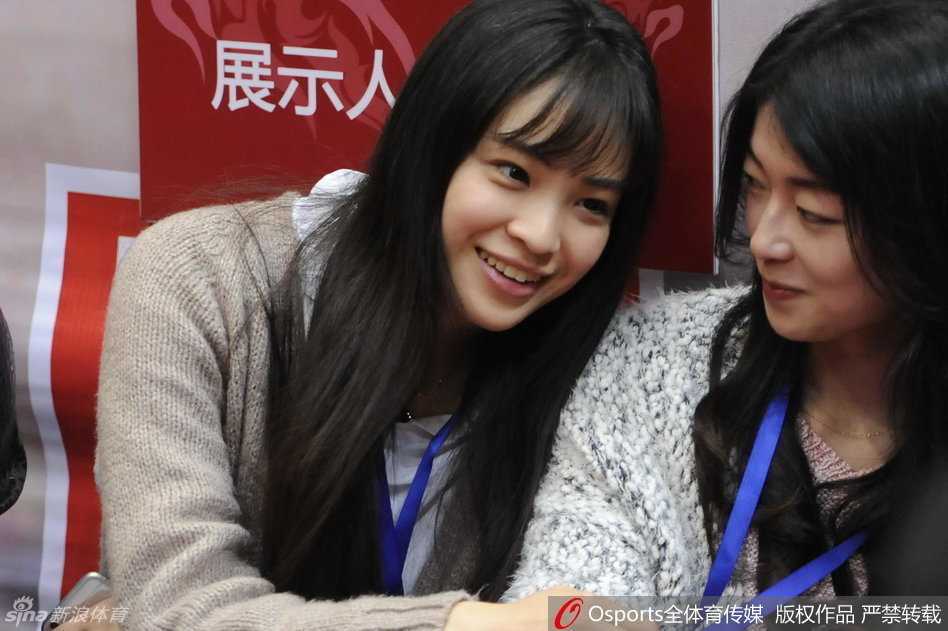 看台上的美女球迷们看到场边趣事，互相交谈，脸上露出轻松愉快的笑容