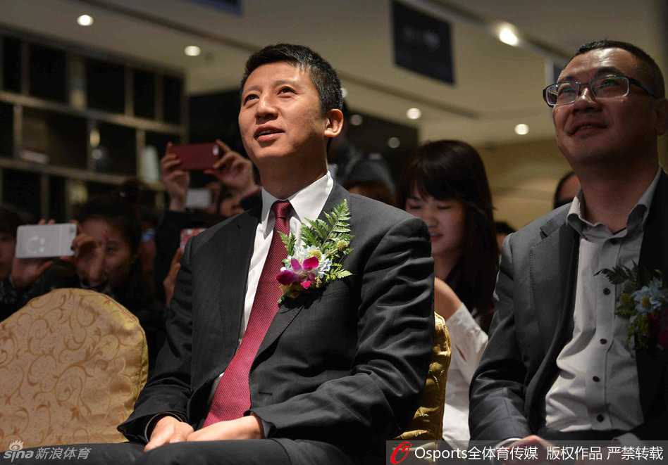 郭士强指导身穿深色运动外套，面带标志性的温和笑容，正俯身为一位小球迷在篮球上签名，周围挤满了充满期待的孩子们