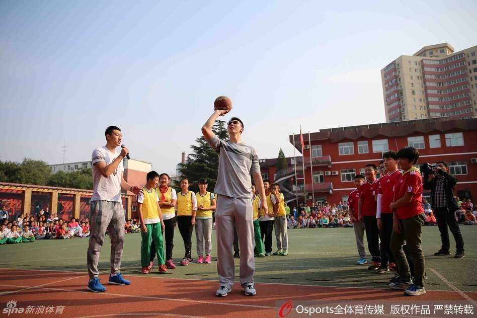 翟晓川站在篮下耐心教一位小朋友投篮姿势，手把手帮助孩子瞄准篮筐，孩子的脸上写满了认真与兴奋