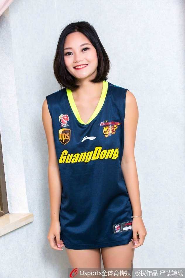 CBA广东主场最美风景线:篮球宝贝球衣写真点燃赛场激情 女孩蹲坐在场边的广告牌旁,单手托腮,宽松的球衣下露出灿烂的笑容,甜美可爱的气质成为赛场边的一抹亮色。