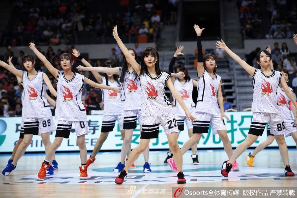 镜头特写一位GNZ48成员，她手持啦啦队花球，专注的眼神中透露出对舞台的热爱，背后是宏远主场巨大的LED屏和热情的观众席。