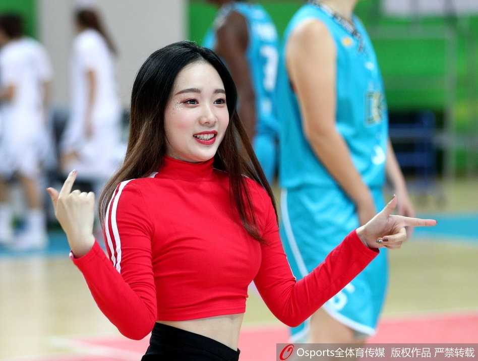 镜头拉近，一位领舞的宝贝正对着观众席绽放自信的笑容，她手中的花球在空中划出优美的弧线，仿佛在邀请全场观众一起加入这场篮球派对。