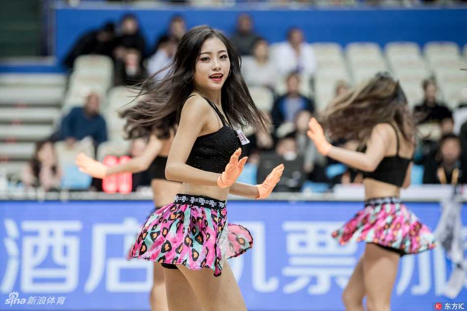 舞蹈进行到高潮部分，两名拉拉队员面对面热舞，她们的动作充满张力与默契，飞扬的发丝和自信的笑容在灯光下闪闪发光，展现出职业拉拉队的专业素养和青春活力。