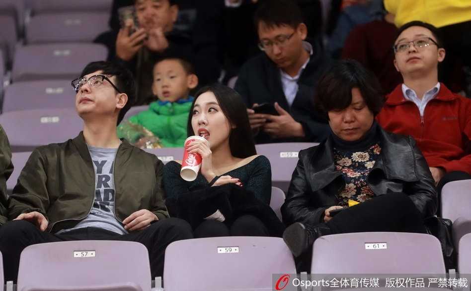 一位身穿白色休闲服的清秀女球迷，双手轻托脸颊，目光专注地望向赛场方向，眼神中流露出对比赛进程的紧张与期待。