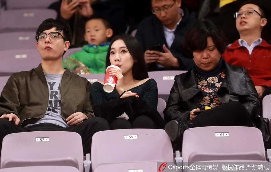 长发飘飘的牛仔衣女球迷，在暖色灯光下侧颜精致，她正神情激动地为场上队员的精彩发挥鼓掌叫好。