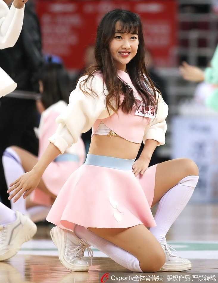 三位篮球宝贝在场地中央摆出俏皮的结束造型，她们的笑容极具感染力，身后的CBA广告牌和欢呼的观众虚影，共同构成了赛场独特的风景线。