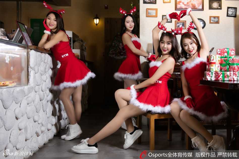 京城篮球宝贝的圣诞魔法:北控啦啦队节日温情瞬间 在明亮的体育馆通道内,一名啦啦队员双手抱满了装满礼物的红色袋子,对着镜头露出俏皮而神秘的表情,仿佛在告诉球迷们:“猜猜里面有什么惊喜?”红色的裙摆与节日的氛围相得益彰。