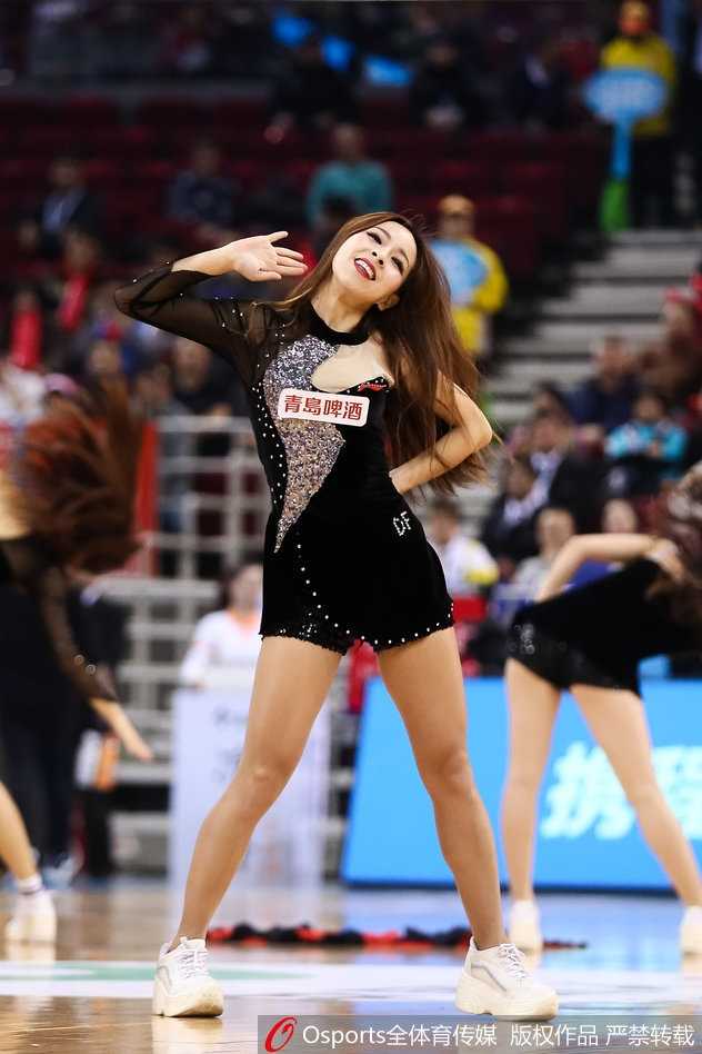 一名领舞的篮球宝贝在聚光灯下格外夺目，她微侧的脸庞在光影中显得精致立体，飒爽的舞姿中透出一股巾帼不让须眉的英气。