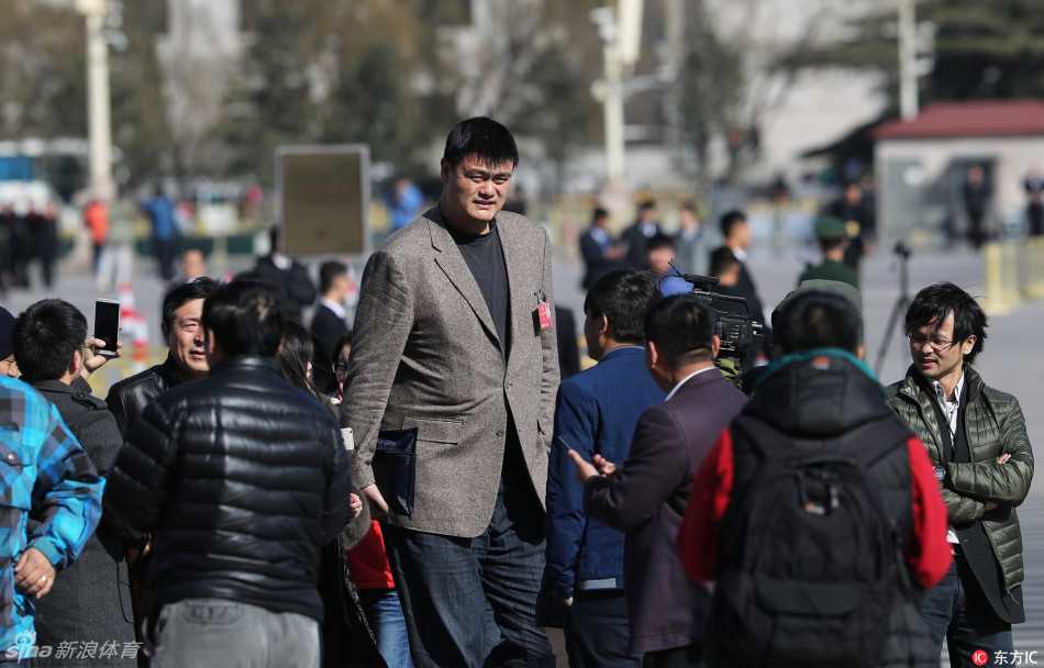 姚明现身NFL超级碗现场，他身着深色西装坐在看台上，周围是山呼海啸的球迷，他则神情专注地关注着场上的逆转大戏。