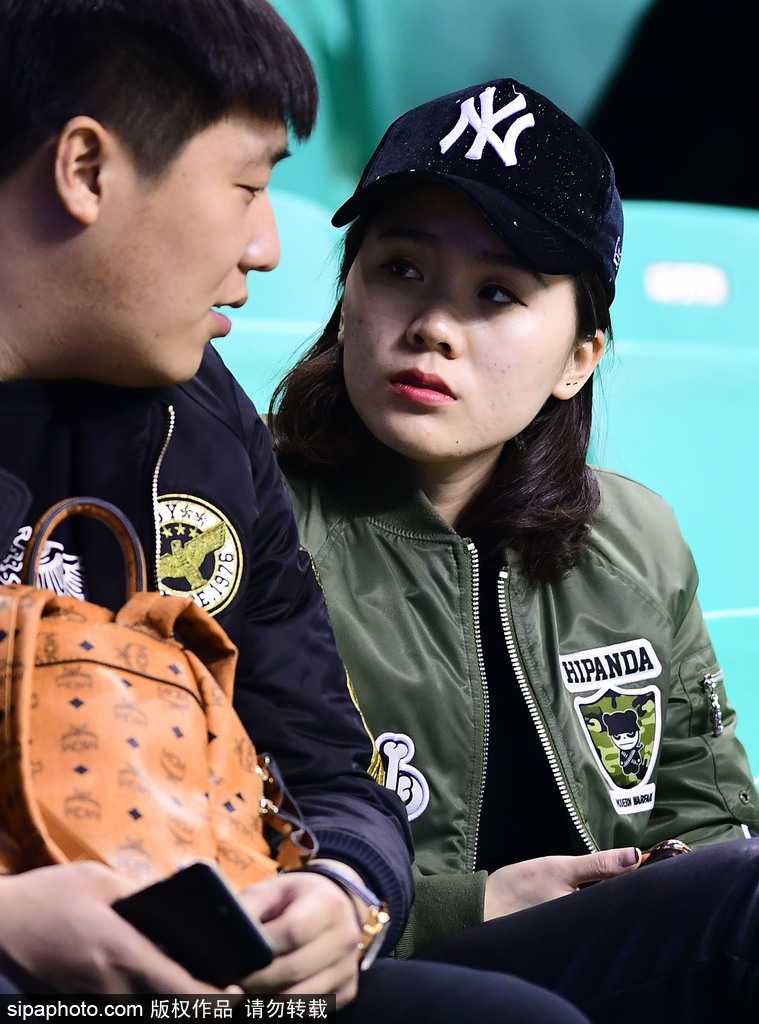 画面中，一位戴着时尚黑框眼镜的女孩，嘴角挂着浅浅的笑意，她并未像周围人那样疯狂呐喊，而是选择了一种安静的陪伴，那份知性的美在激情四溢的球场中显得格外独特，仿佛在用心灵与场上飞奔的球员对话。