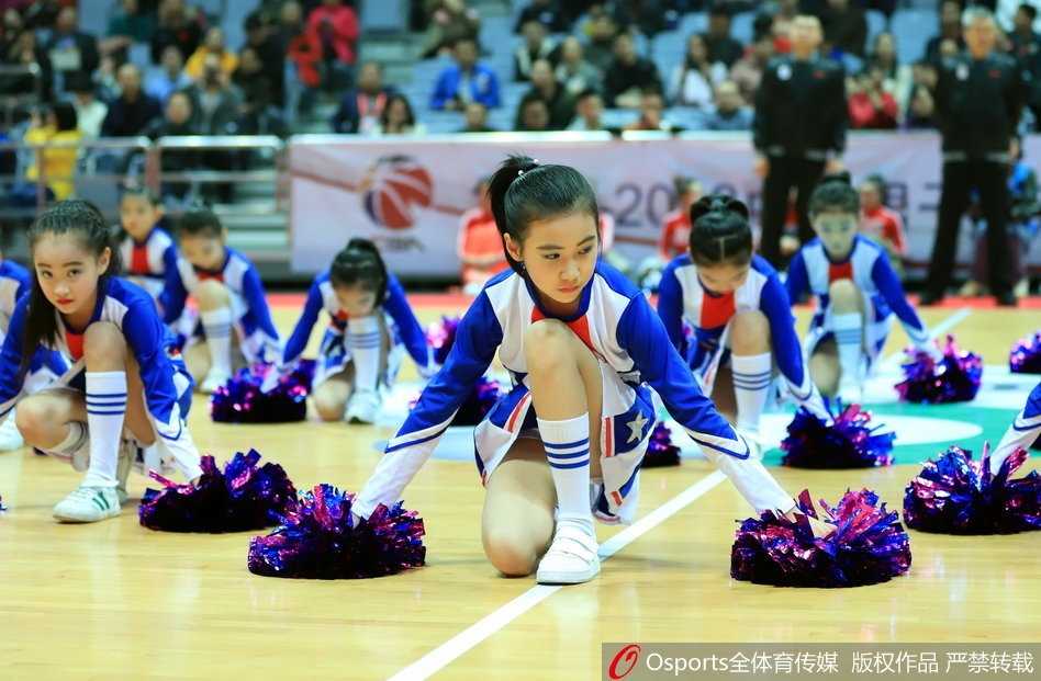 八一篮球小将萌动赛场 活力宝贝诠释篮球未来 几位扎着丸子头的小宝贝身穿红色球衣,手拿金色花球,踮起脚尖认真观看比赛,眼神里满是好奇与兴奋