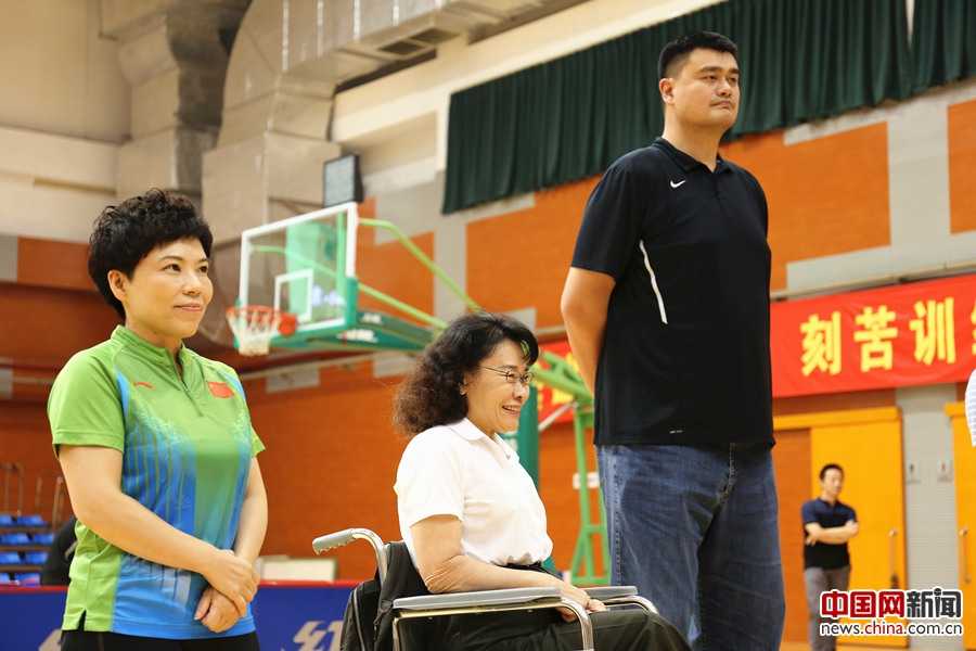 篮球巨人姚明微笑着站在轮椅篮球选手中间，他俯下身子与坐轮椅的运动员平视交谈，巨大的身高差构成了画面中最温柔的尊重与鼓励