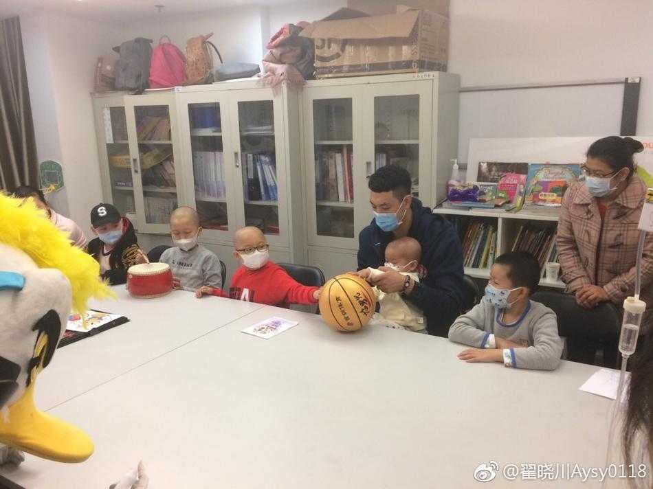 身穿红色球衣的翟晓川俯身蹲在病床前，他与戴着口罩的小朋友额头轻轻相贴，用无声的肢体语言传递着勇气与关爱，画面温馨感人。