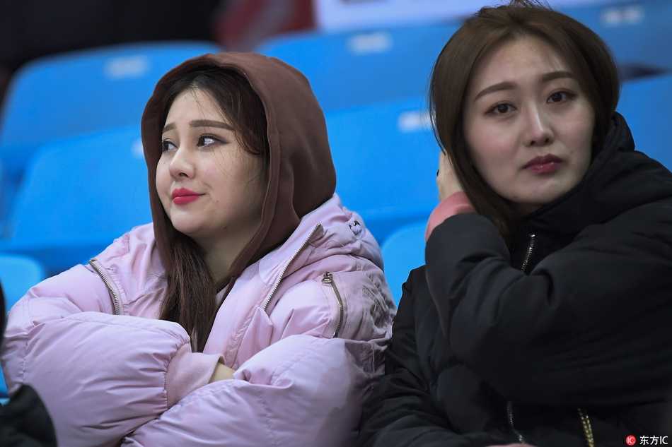 冰雪赛场上的靓丽风景线 吉林女球迷点燃寒冬激情 身穿白色短款羽绒服的清纯女生,手拿吉林东北虎的加油棒,眼神清澈地望向赛场方向,嘴角带着浅浅的笑意,仿佛对主队充满信心