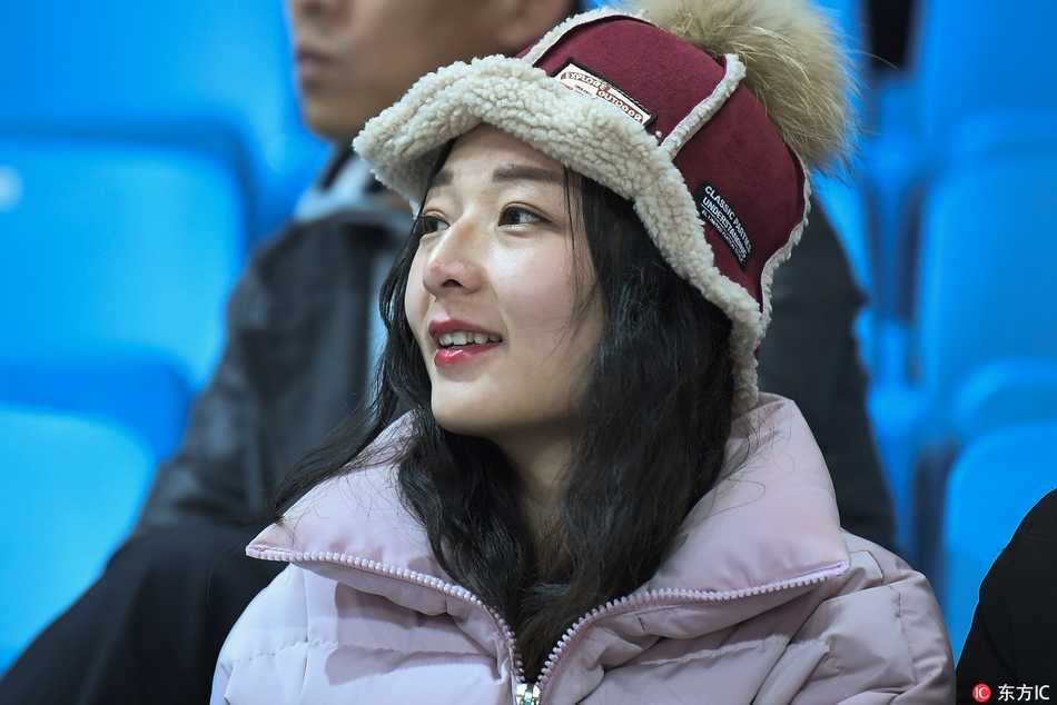 冰雪赛场上的靓丽风景线 吉林女球迷点燃寒冬激情 一位戴着时尚毛线帽的女生侧身回眸,长长的睫毛和精致的侧颜在体育馆的灯光下显得格外动人,身后是模糊的座位和人海,宛如电影画面