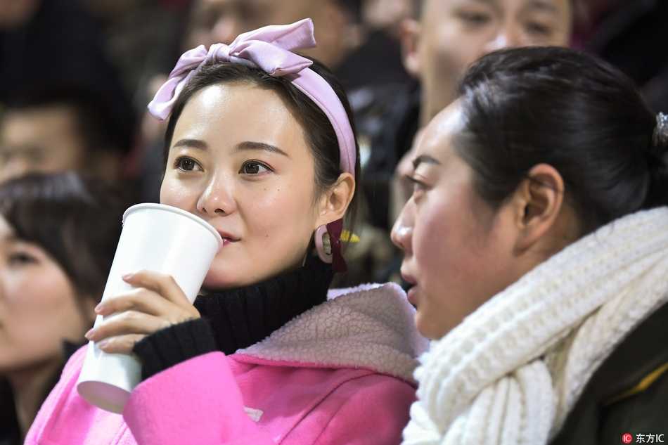 冰雪赛场上的靓丽风景线 吉林女球迷点燃寒冬激情 一位穿着黑色长款大衣的气质美女,双手揣在兜里,静静站立在看台过道,眼神中带着一丝疏离感,颇有大片街拍的风范,尽显高冷女神范