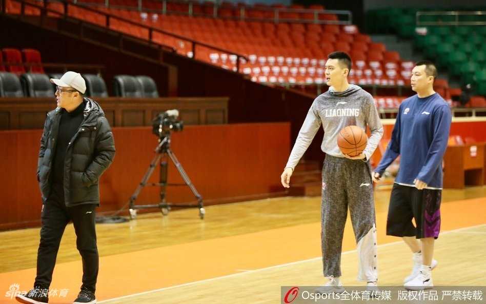 杨鸣身披辽宁队训练服，在山东主场训练馆内眉头紧锁，目光直视前方，周围队友神情严肃，空气中弥漫着紧张对峙的气息。